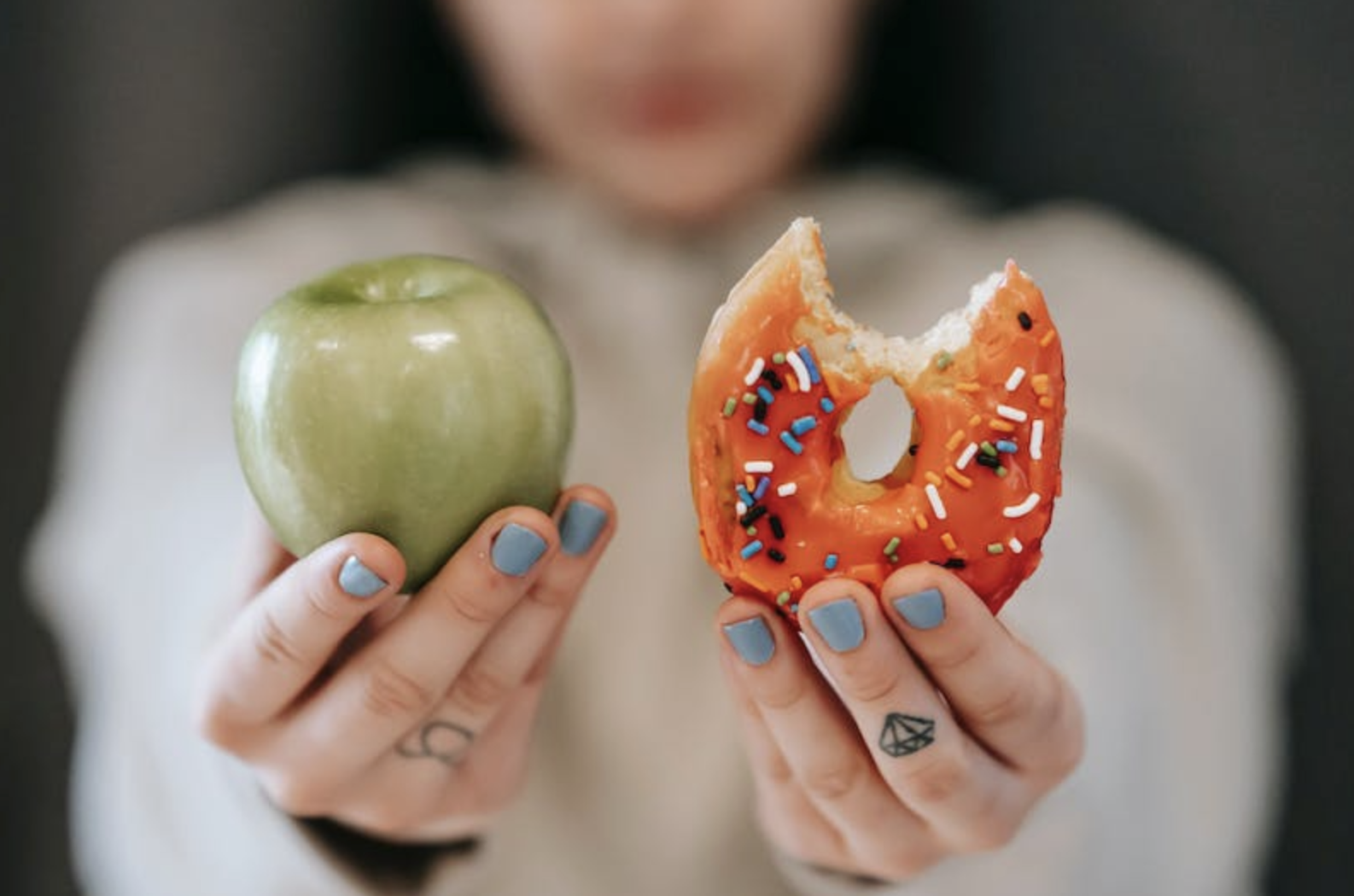 a woman holding a green apple and a doughnut with a bite